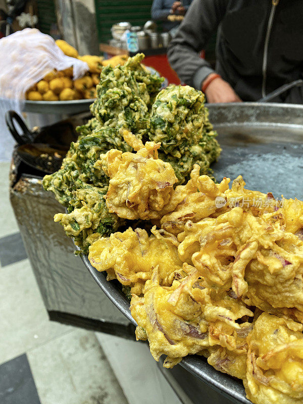 一堆酥脆的洋葱bhajis和palak pakora(菠菜馅饼)放在不锈钢的塔利(托盘)上，印度街头美食素食小吃，高架视野，重点放在前景